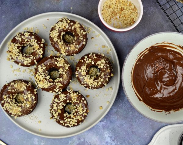Image of some nutty chocolate orange doughnuts on a plate. To the right is a bowl of melted chocolate.