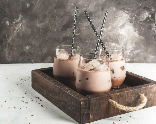 An image of three vegan oat m!lk iced hot chocolates in tumblers on a wooden tray