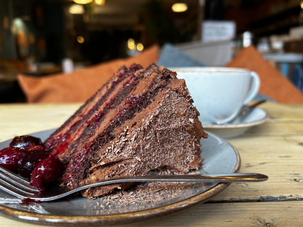 Fudgy slice of cherry chocolate Matilda cake with glossy dark chocolate frosting and layers of cherry compote