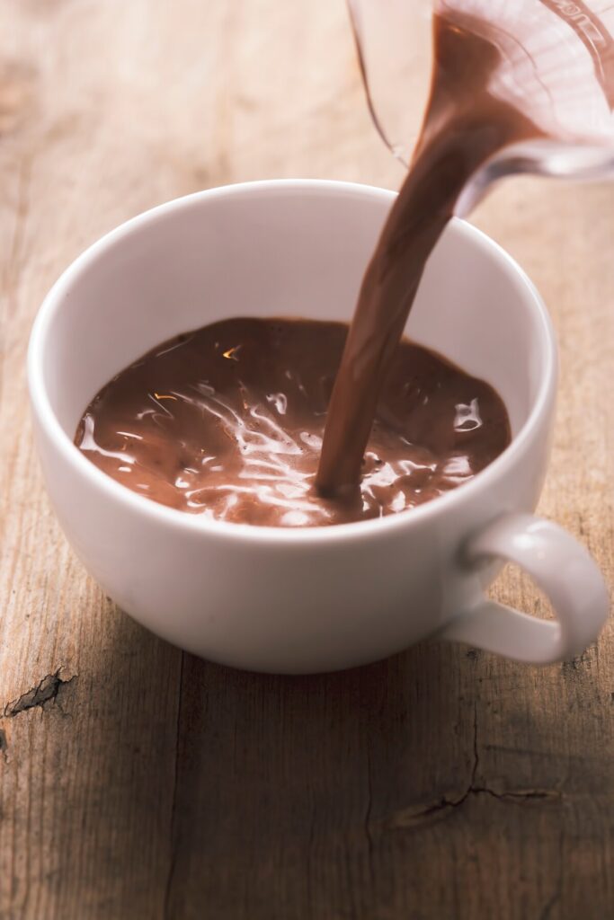 Thick, glossy Spanish-style hot chocolate being poured into a white mug on a wooden table